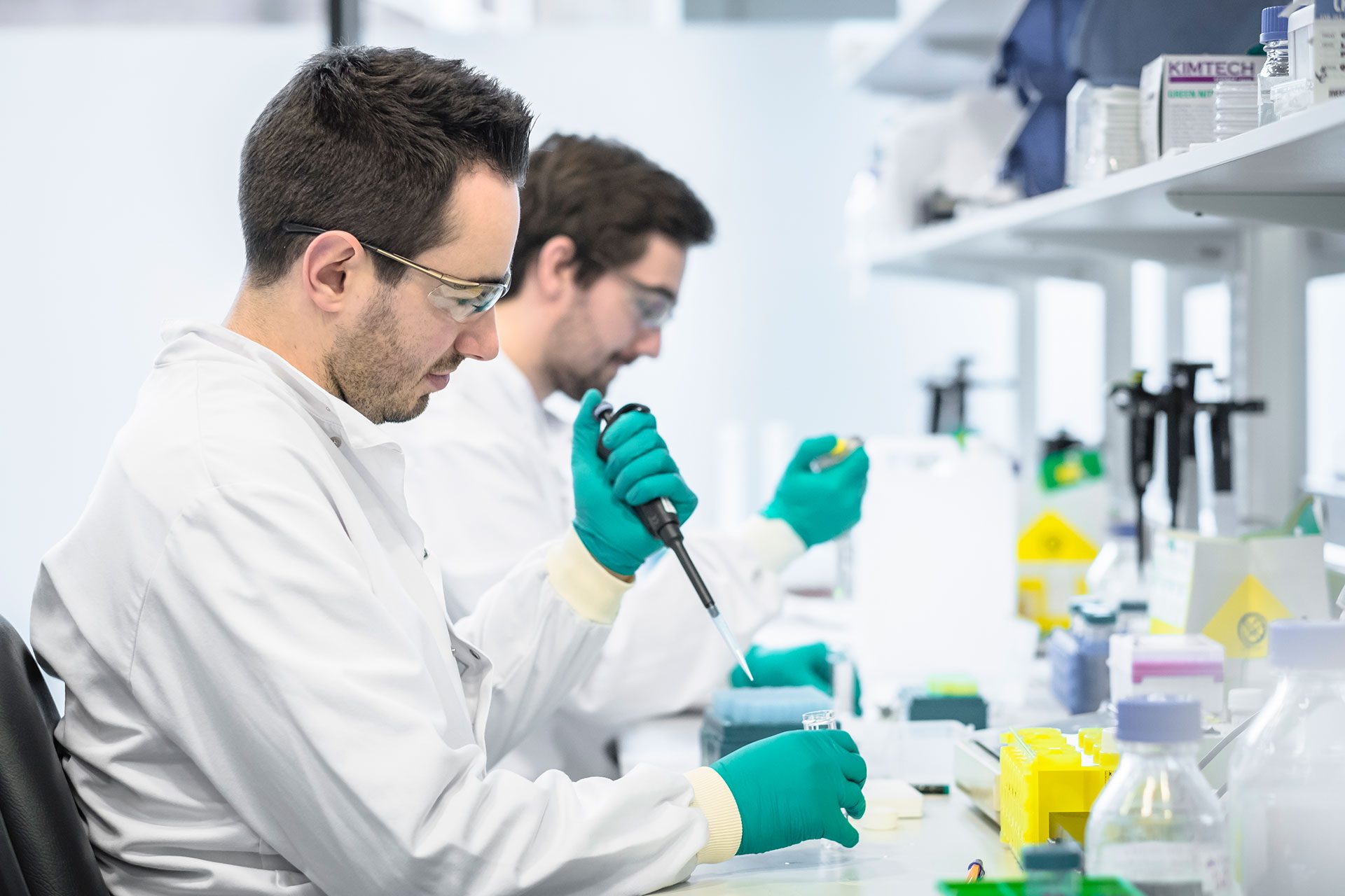 People wearing lab coats, using pipettes to drop liquid into test tubes.