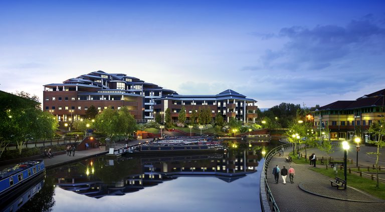 Office building next to a canal. The streetlights reflect in the still water of the canal.