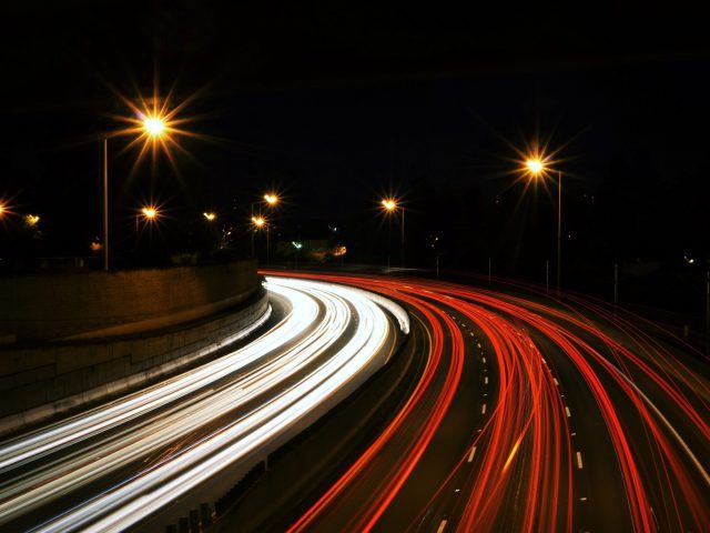 Highway at night with headlights and brake lights forming white and red light trails.