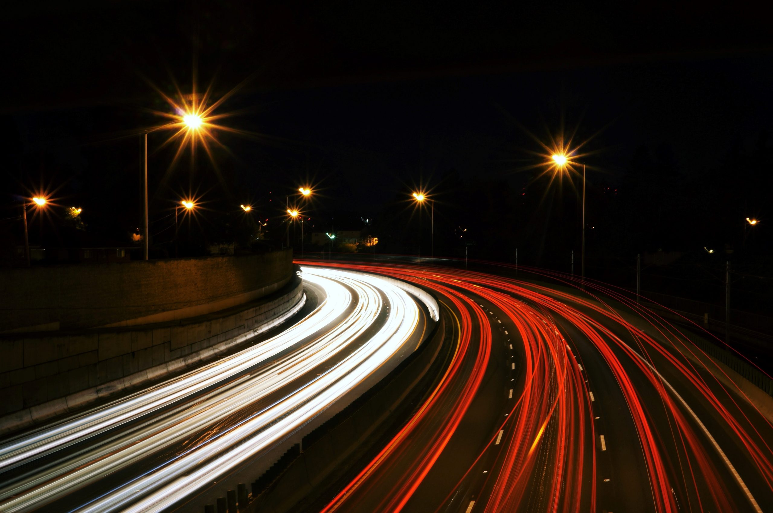 Highway at night with headlights and brake lights forming white and red light trails.
