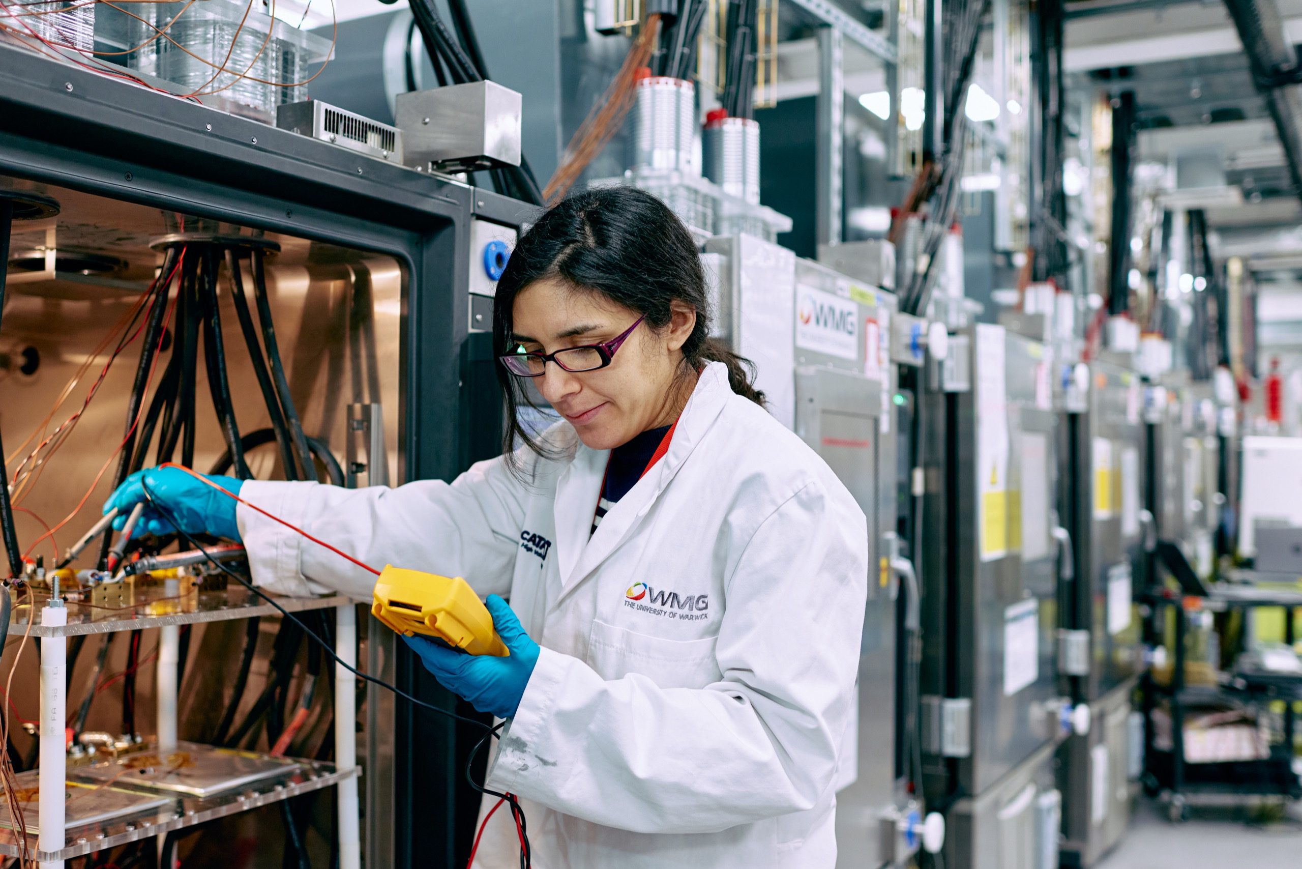 Person in a lab coat checking machinery using a hand held device.