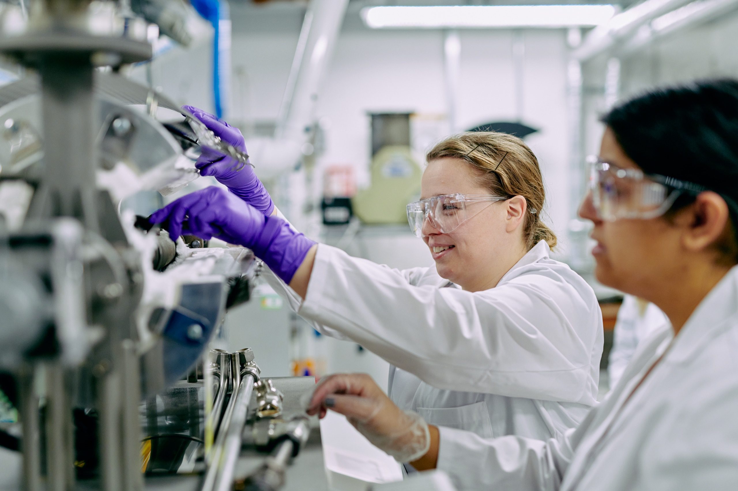 People wearing lab coats and safety goggles changing settings on a machine.