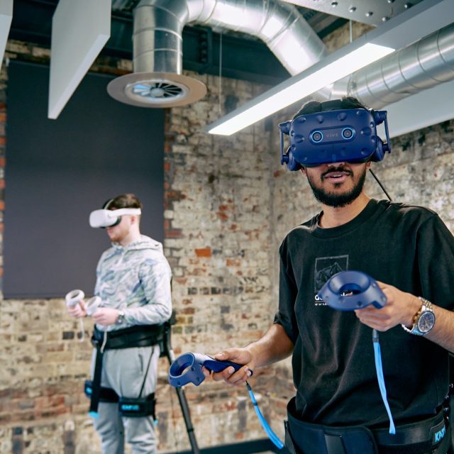 Two people wearing VR headsets and handheld controllers.