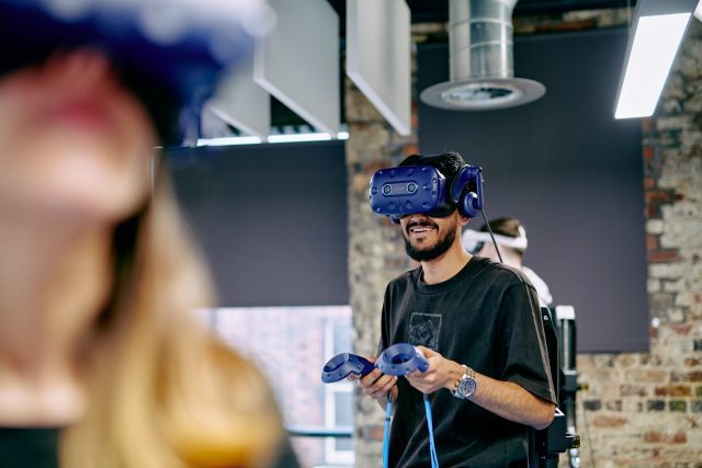 A man wearing a VR headset with 2 handheld controllers shaped like rings.