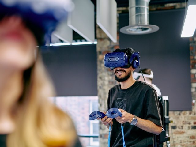 A man wearing a VR headset with 2 handheld controllers shaped like rings.