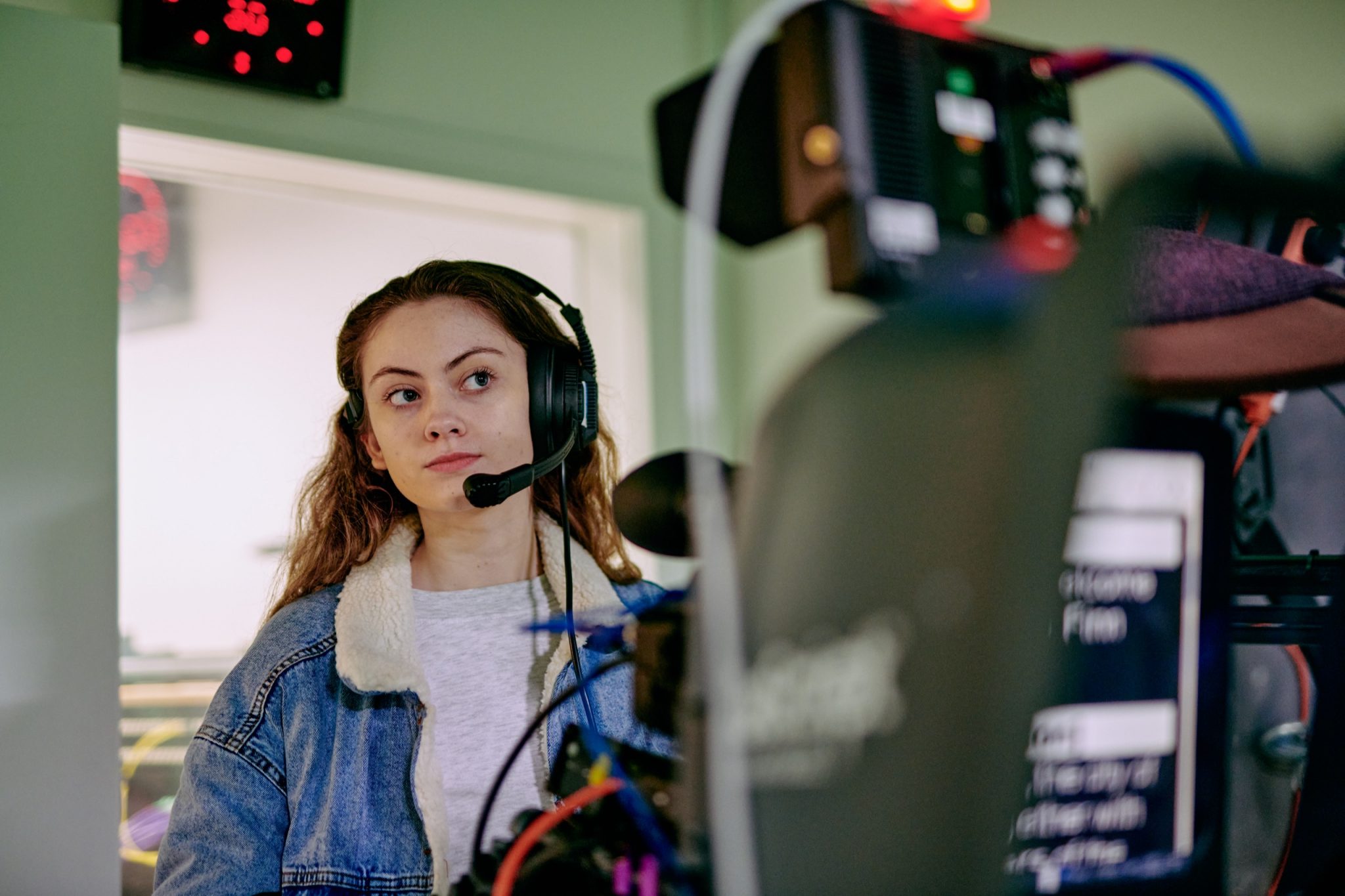 A woman wearing a headset with microphone. Blurry cameras are visible in the foreground.