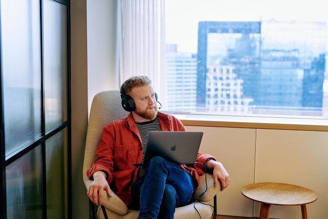 Man sitting cross legged with a laptop and headset on. Collaborative working at Alpha Works, Birmingham.