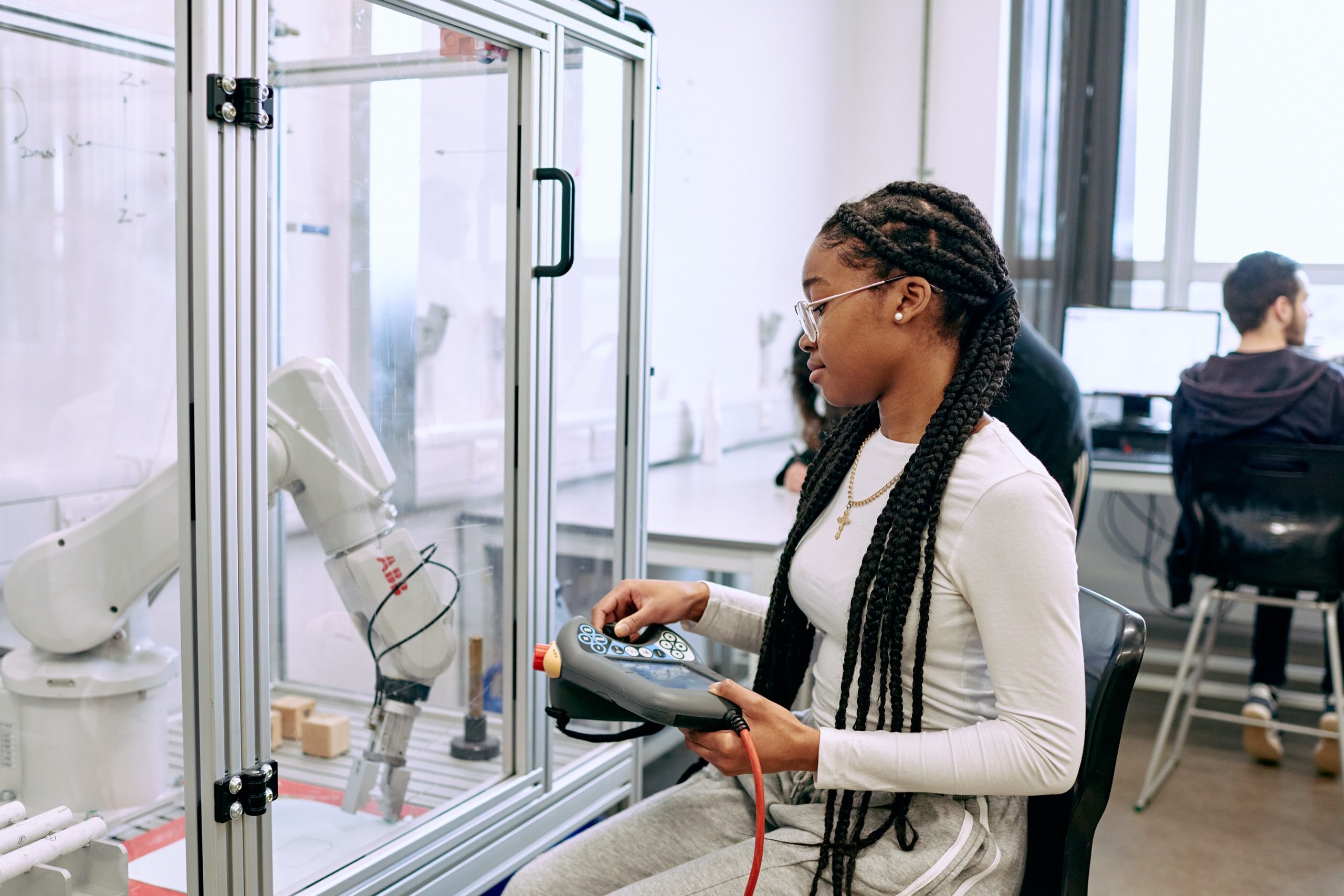 A woman uses a controller pad to move a robotic arm in a glass box.