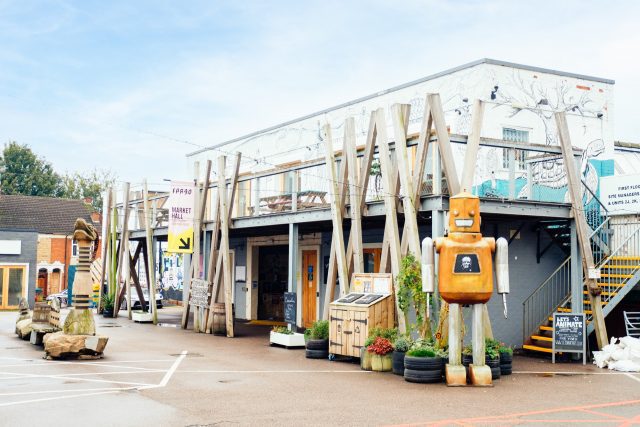 Wooden robot statue outside a funky store. A sign pointing to it reads 'Market Hall'.