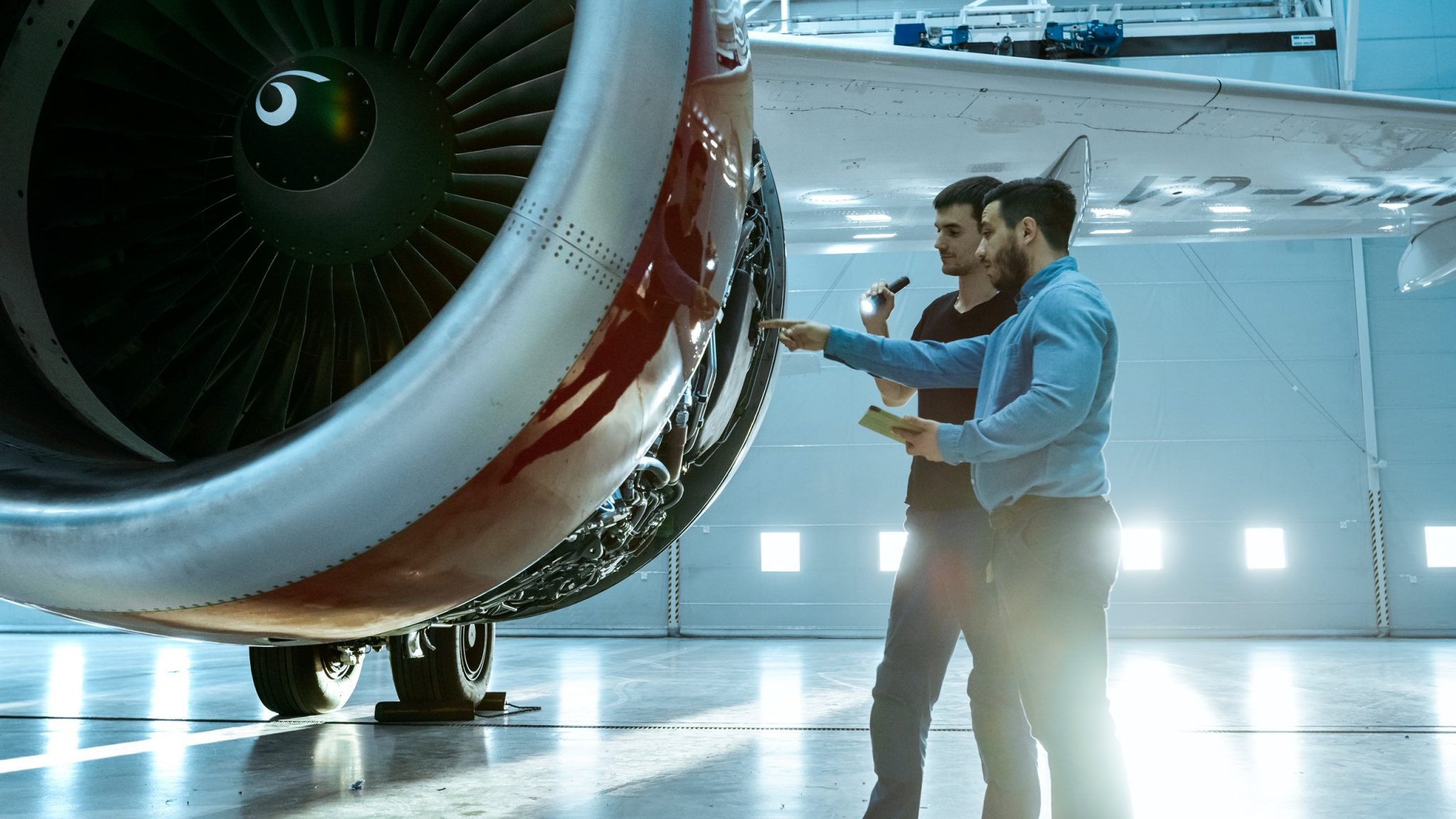 A jet engine with the outside panel open. People are inspecting various parts of the inner engine.