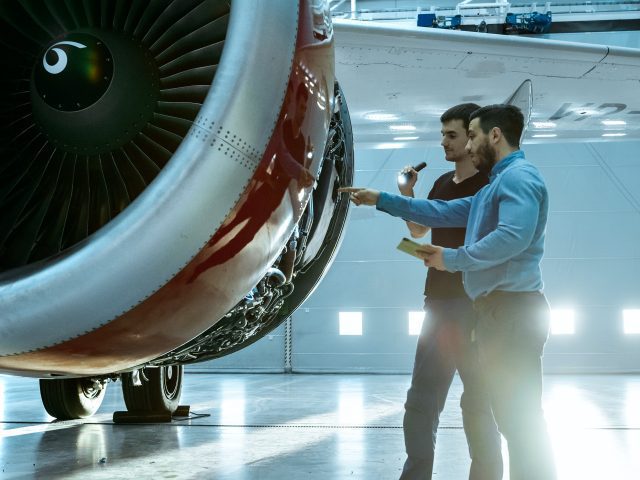 A jet engine with the outside panel open. People are inspecting various parts of the inner engine.