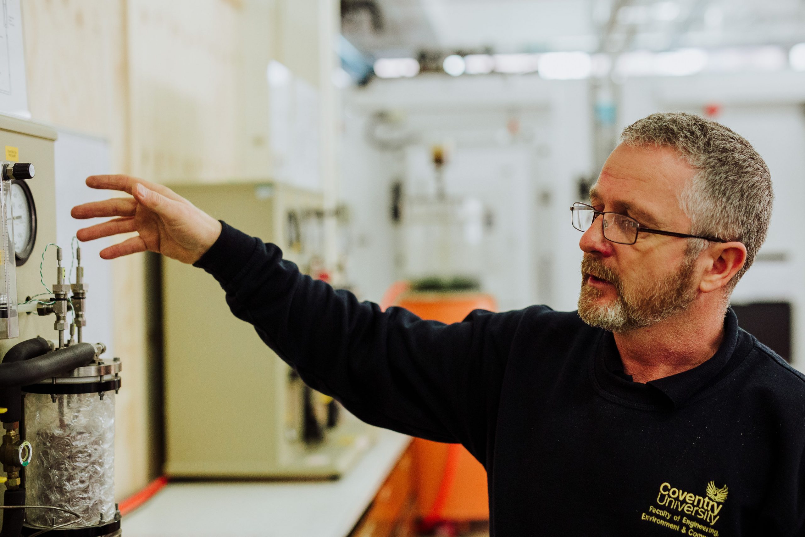 A man wearing a Coventry University jumper, points at something on a shelf.