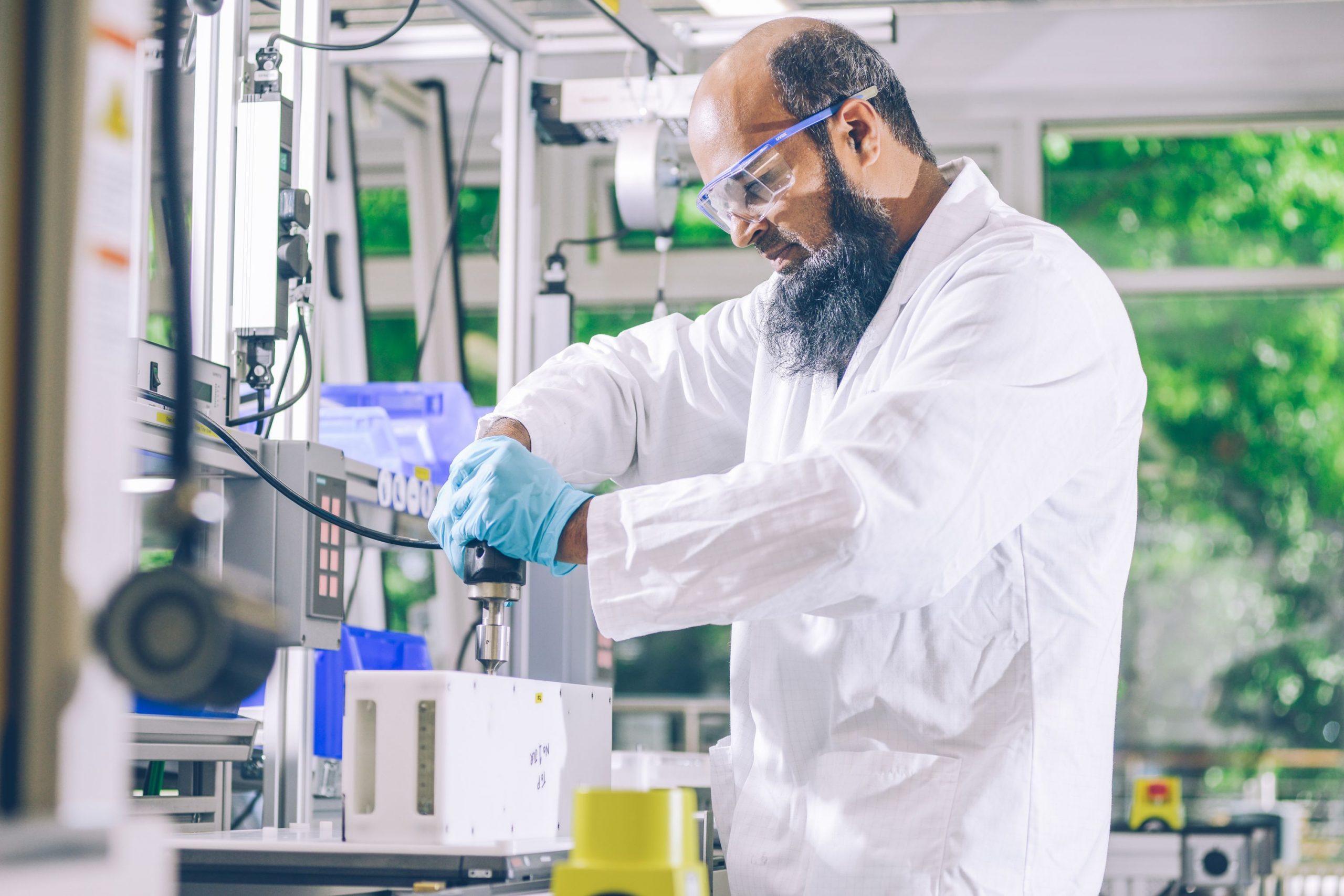 Person in a lab coat machining a plastic rectangle on the desk.