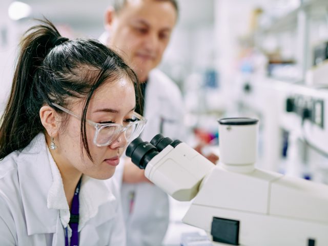 Students inspecting Cancer cells under microscope.