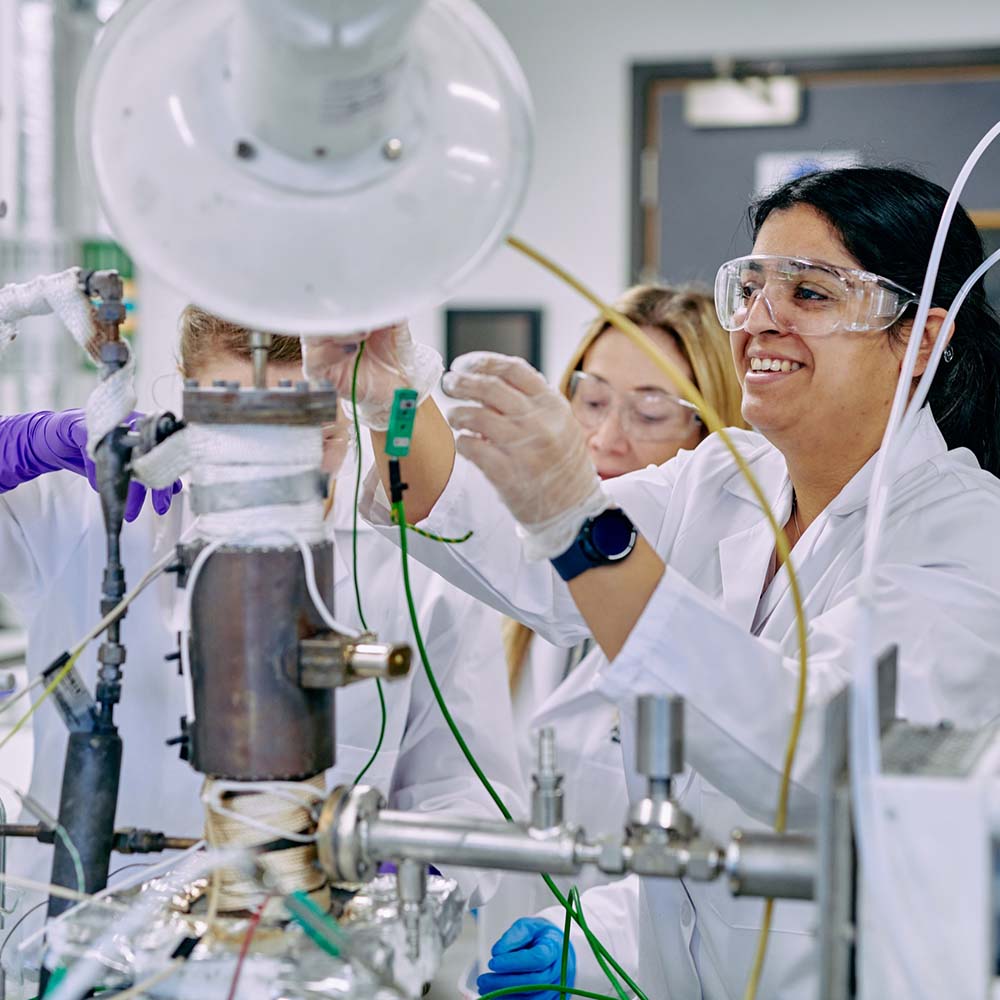 People wearing safety goggles, lab coats and disposable gloves, setting up some machinery on a desk.