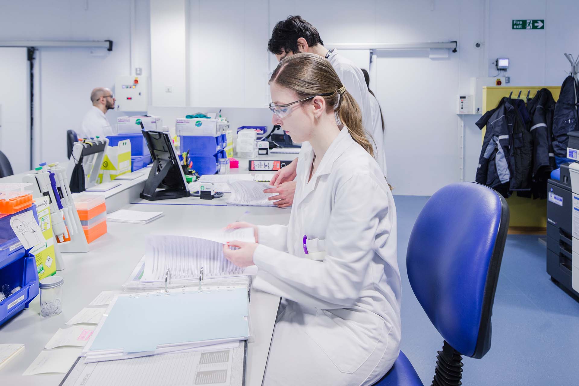 People in lab coats and safety goggles reading binders of information.