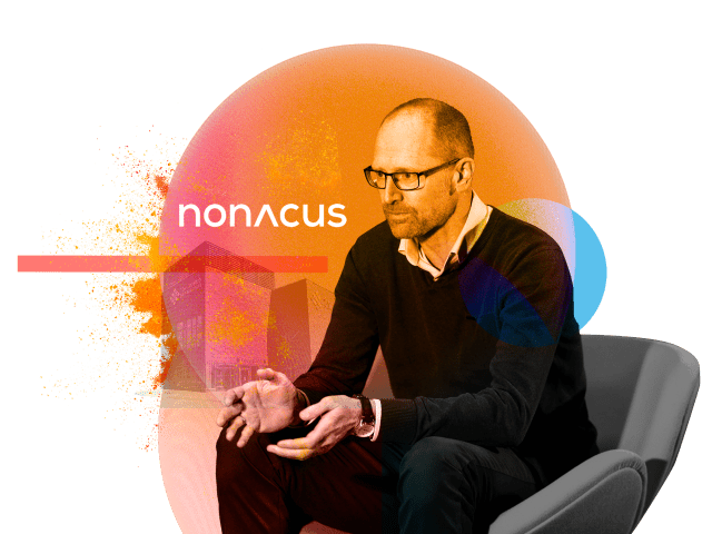 Chris Dale of Nonacus sits in an interview chair with the title of the company behind him.
