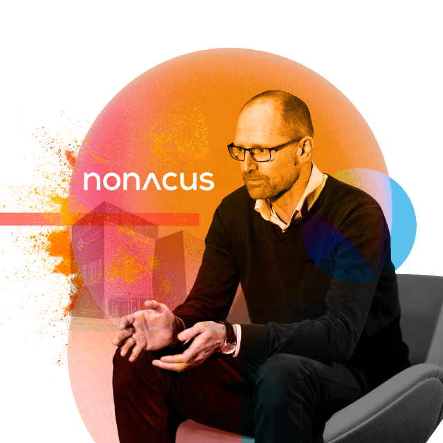 Chris Dale of Nonacus sits in an interview chair with the title of the company behind him.