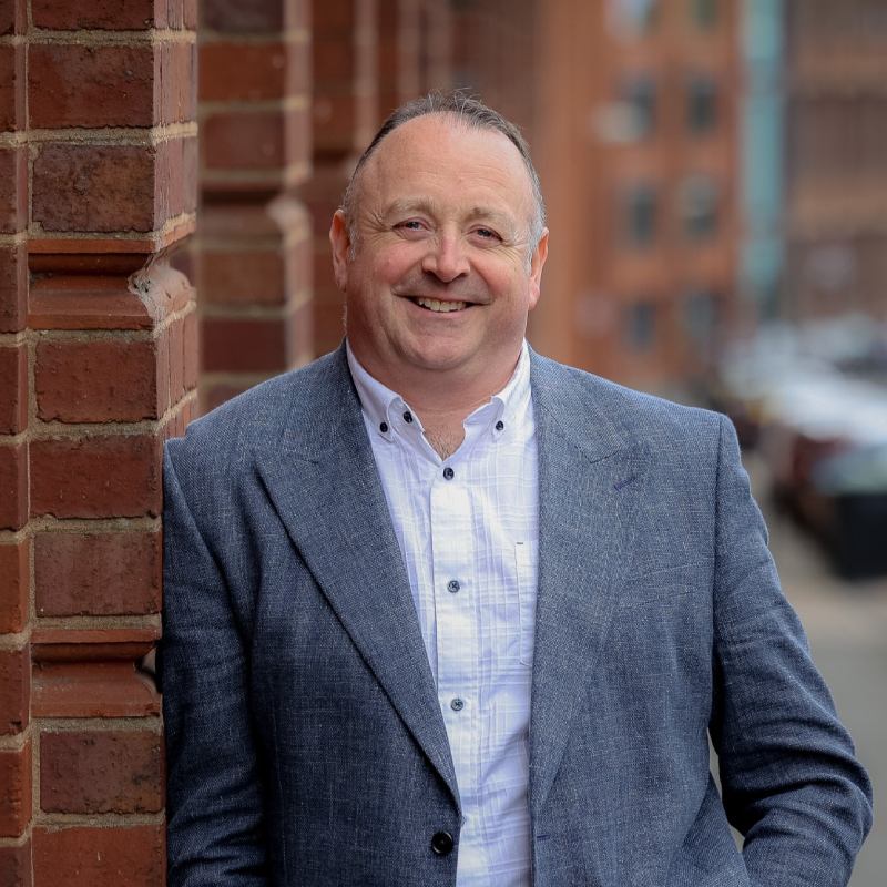 The Director of Pinnegar Hayward Design smiles at the camera as he leans against a wall at the company's location in the Jewellery Quarter